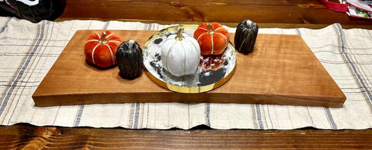 A handmade serving board as a centerpiece on a table with fall-colored pumpkins on top.